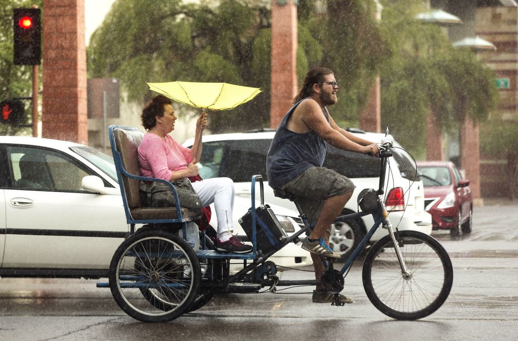 A Pedicab drives down Van Buren Road carrying a woman with a yellow umbrella in the rain on Friday, June 5, 2015 in Phoenix, AZ.