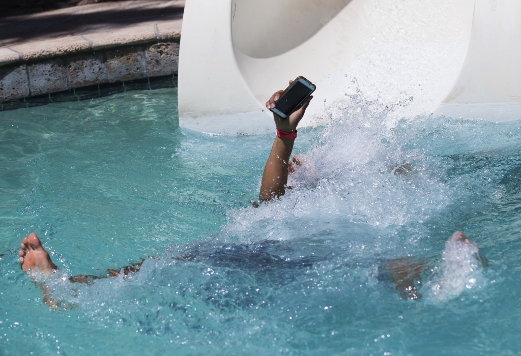 Alex Reyes, 18 from Chandler, keeps his cell phone from going underwater while using the slide at the River Ranch at Pointe Hilton Squaw Peak April 19, 2015.